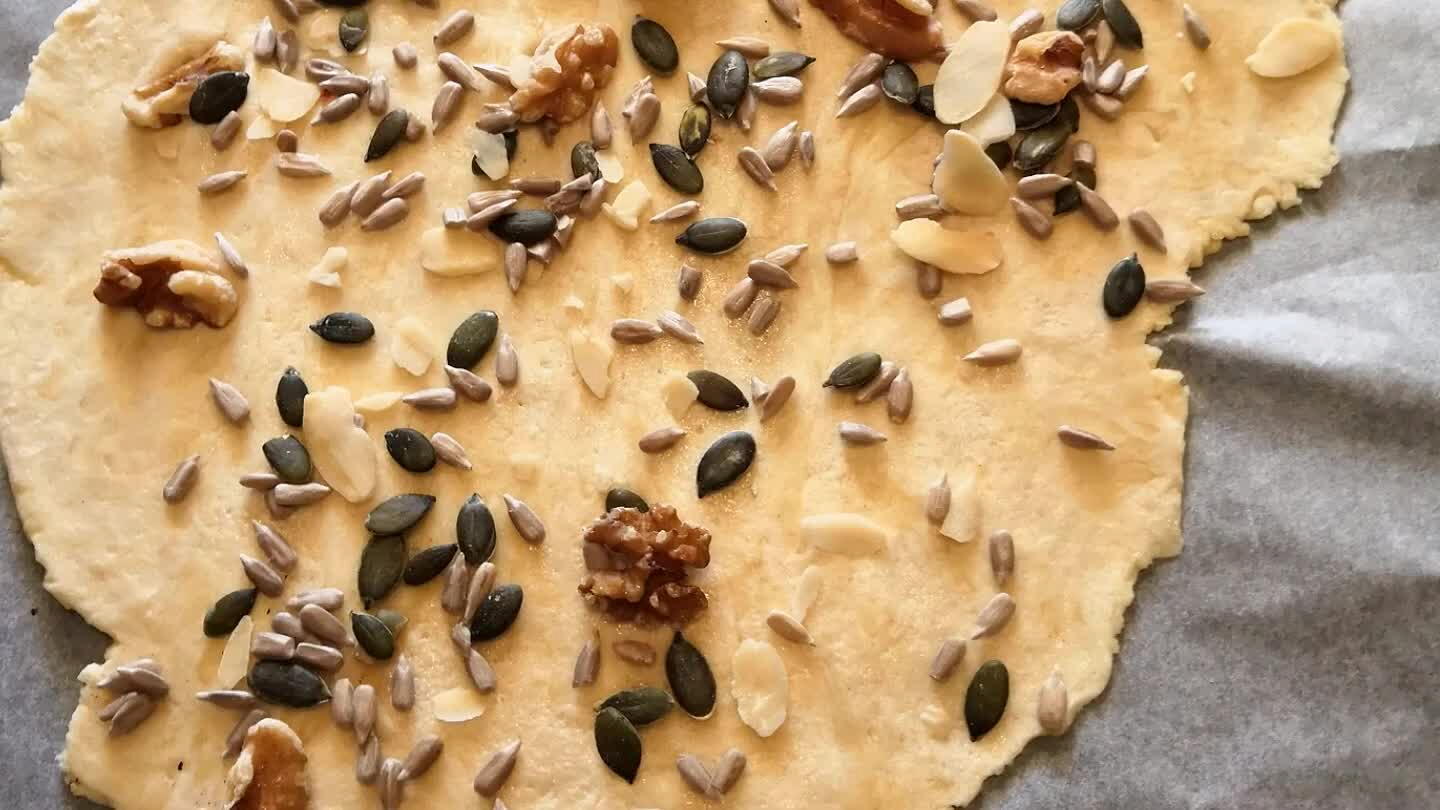 a allo stesso un ulteriore foglio di carta forno, per poi con l'aiuto di un mattarello appiattire il tutto. E guarniamo con i nostri semini e qualche granello di sale.