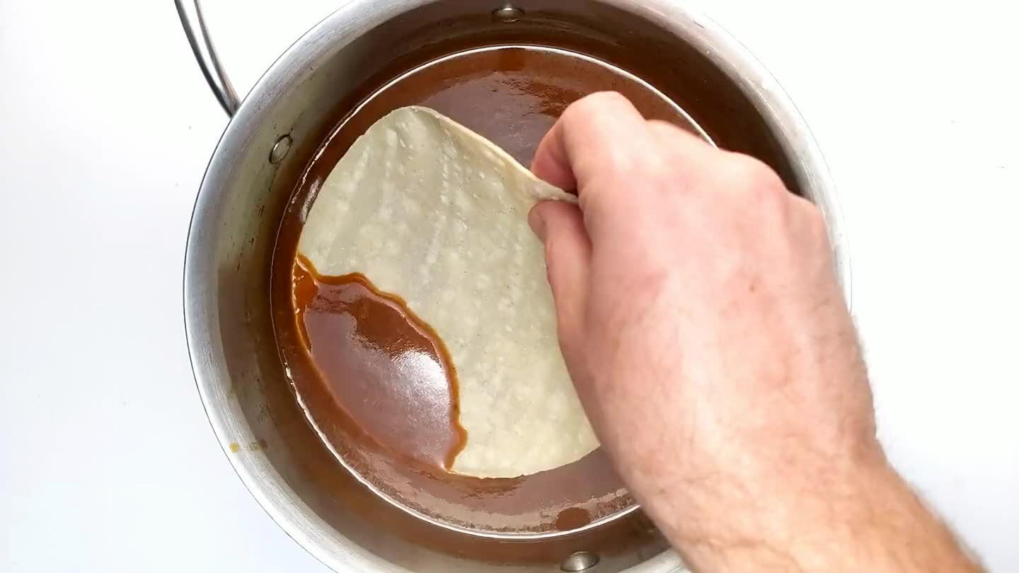 but lets not focus on that. Dunk your tortillas in sauce to warm them up slightly and make them pliable. If you want to take it to the next level here, toast each tortilla in a skillet with a little hot oil before coating in sauce. This improves the texture in my opinion, but adds a lot of prep time.
